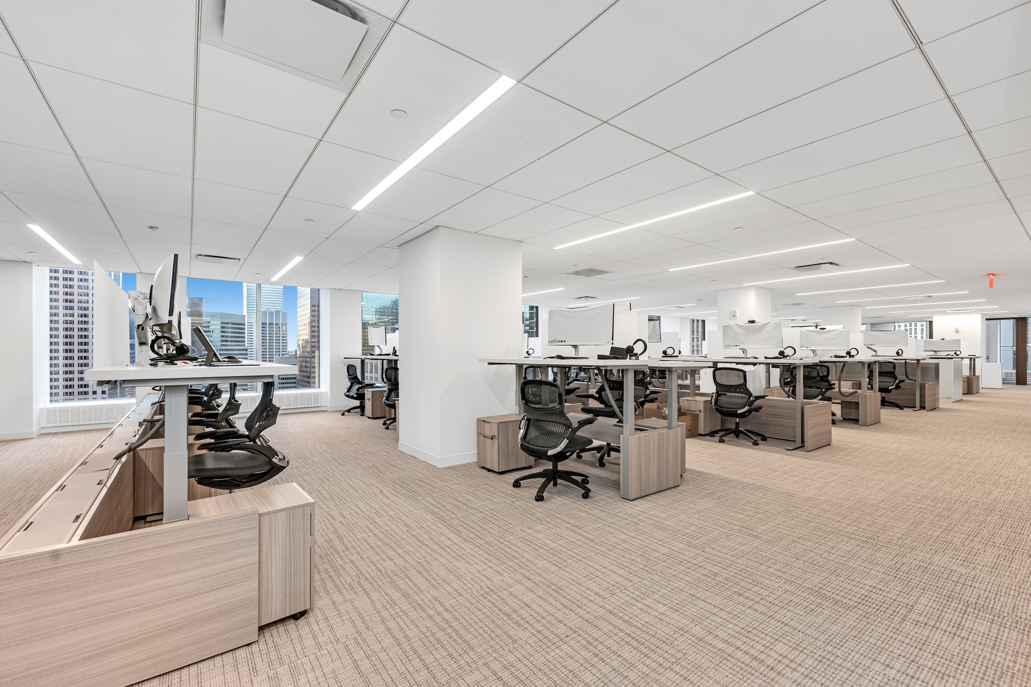Rows of open-plan desks with height-adjustable tables, black mesh chairs, and skyline views