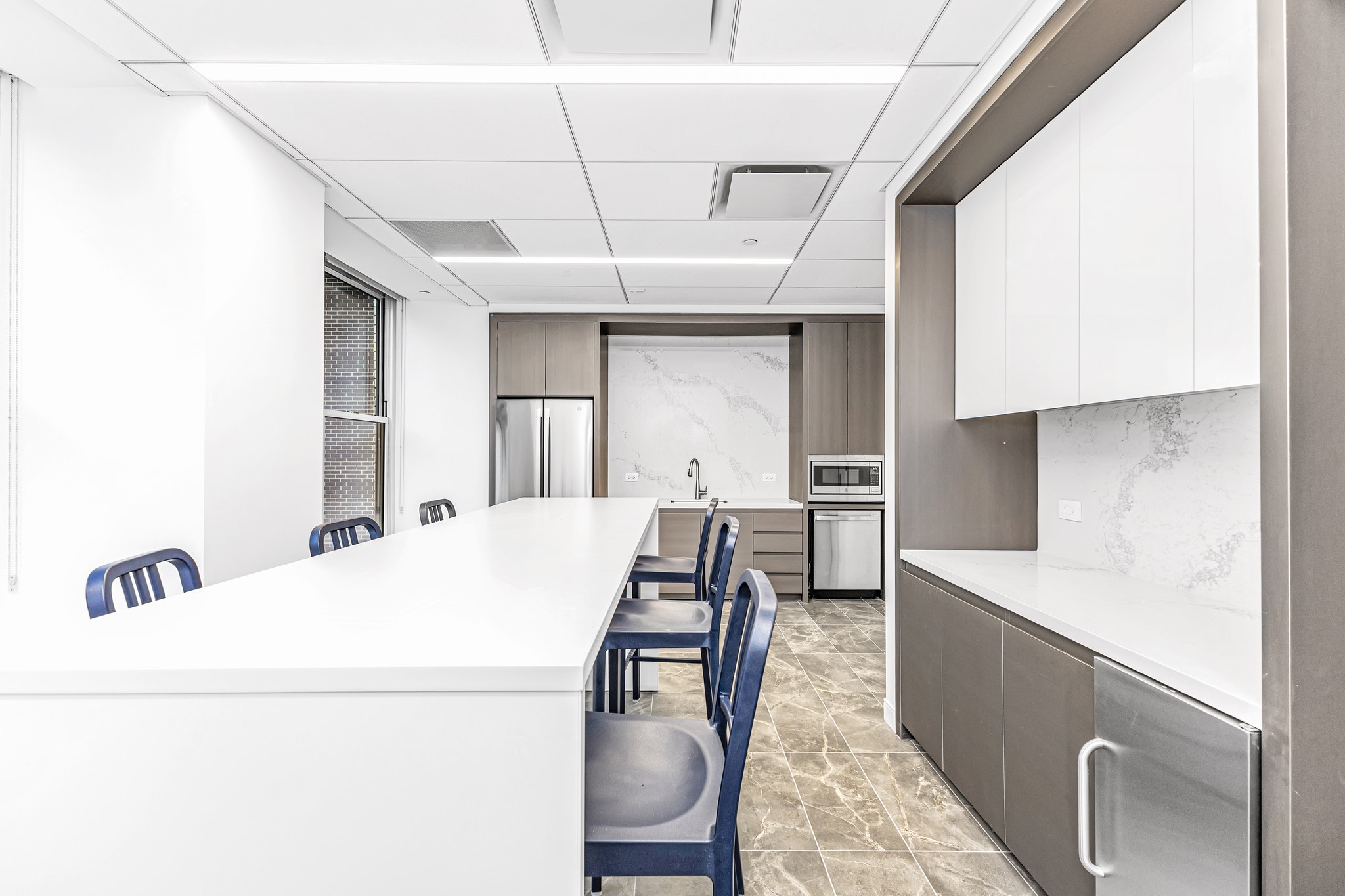 Office pantry with white island, navy stools, stainless appliances, and marble backsplash