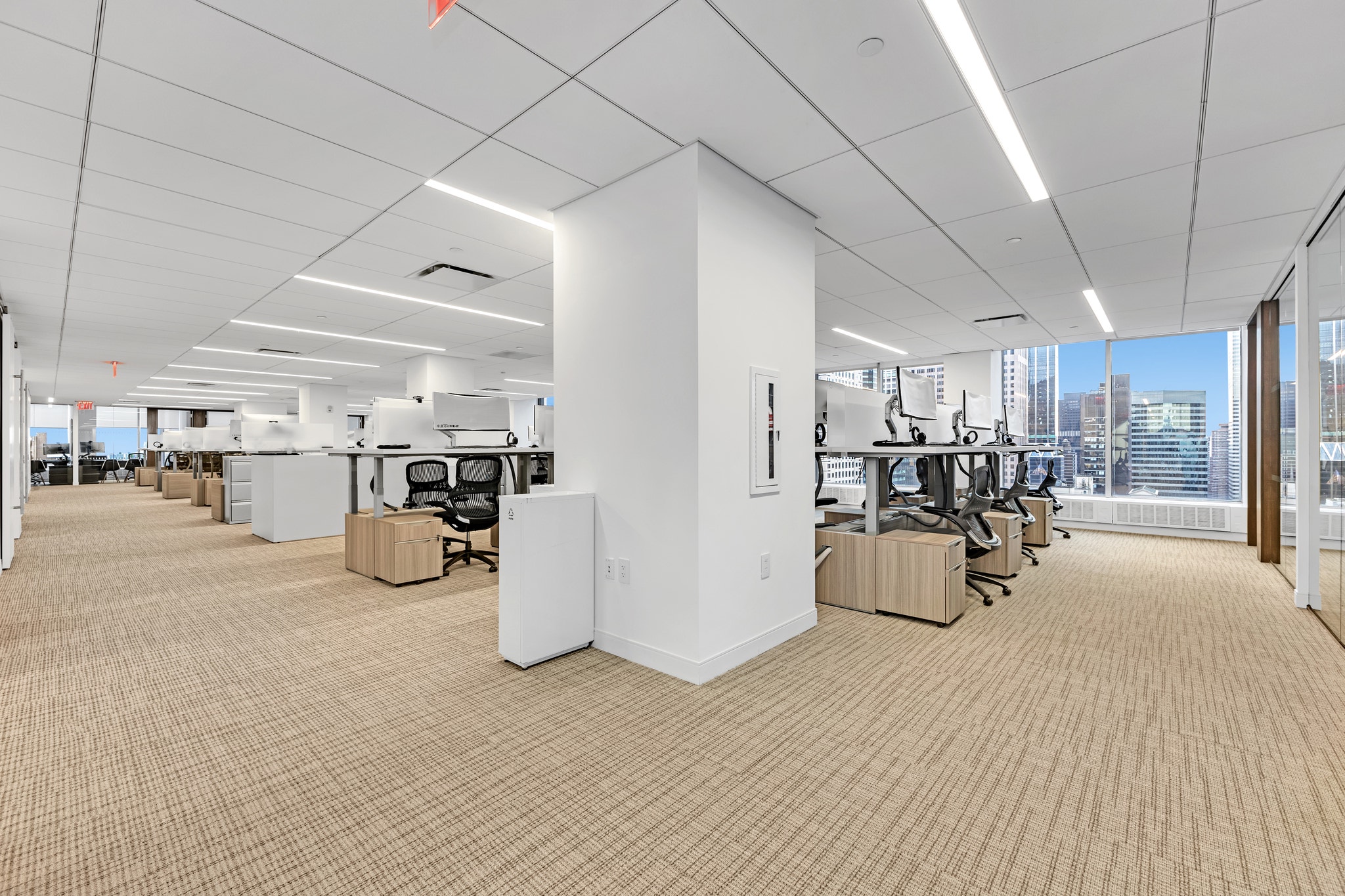 Open office workstations with dual monitors, ergonomic chairs, and floor-to-ceiling city views