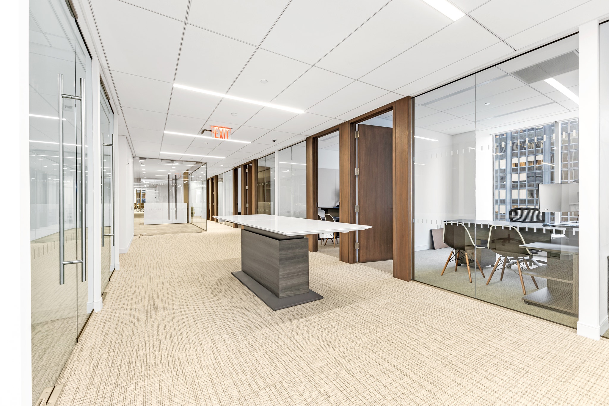 Corridor with dark wood conference room doors, glass partitions, and central white boardroom table