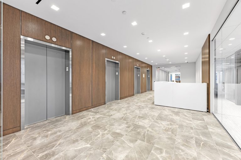 Row of stainless elevator doors along walnut paneled wall with marble floor and reception desk