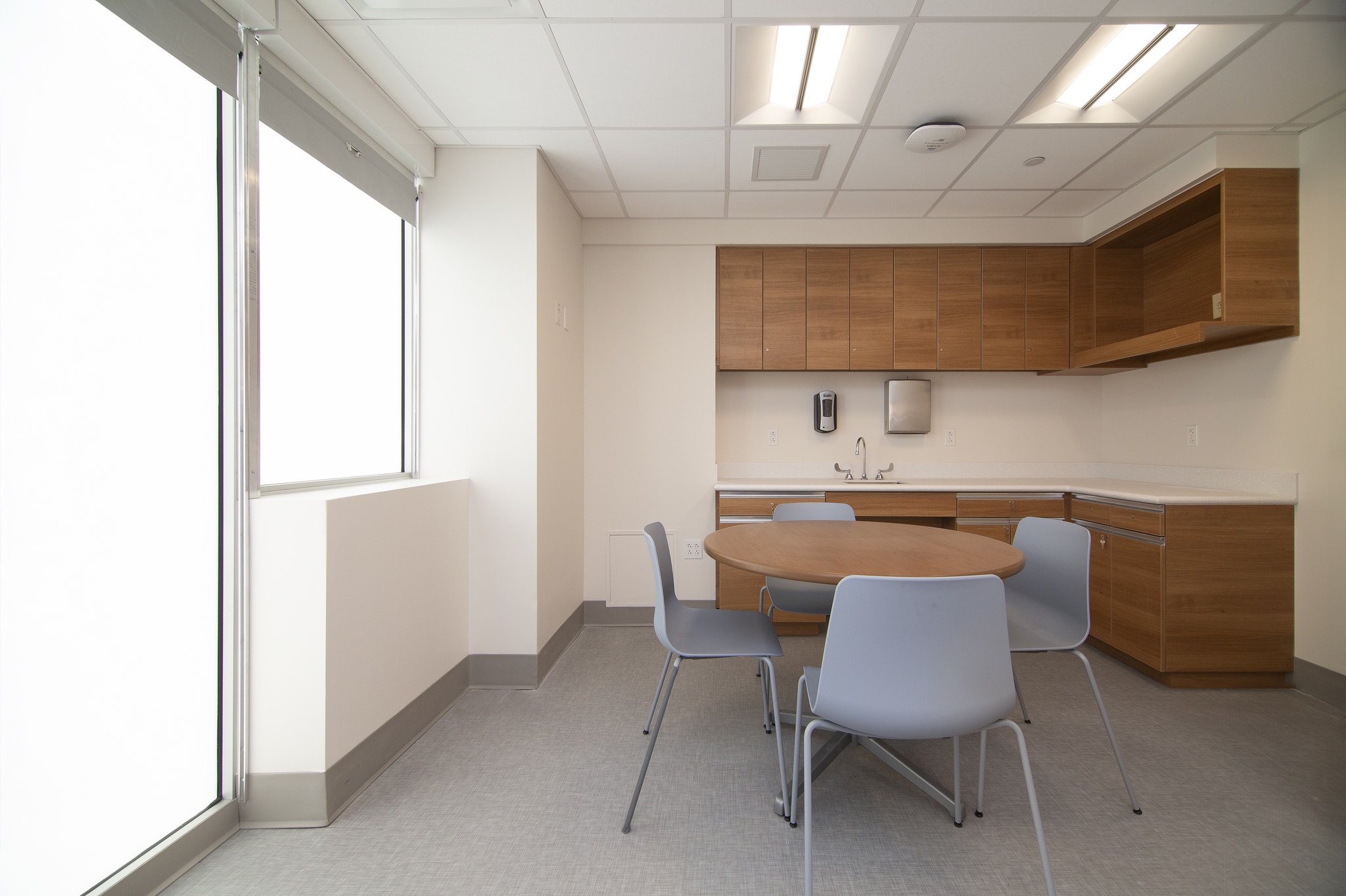 Consultation room with oval wood table, gray chairs, and wall-mounted sink cabinetry
