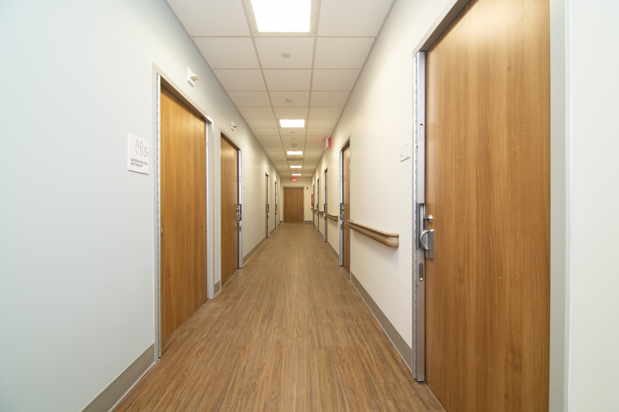 Long corridor with wood doors, handrails, and gender neutral restroom signage