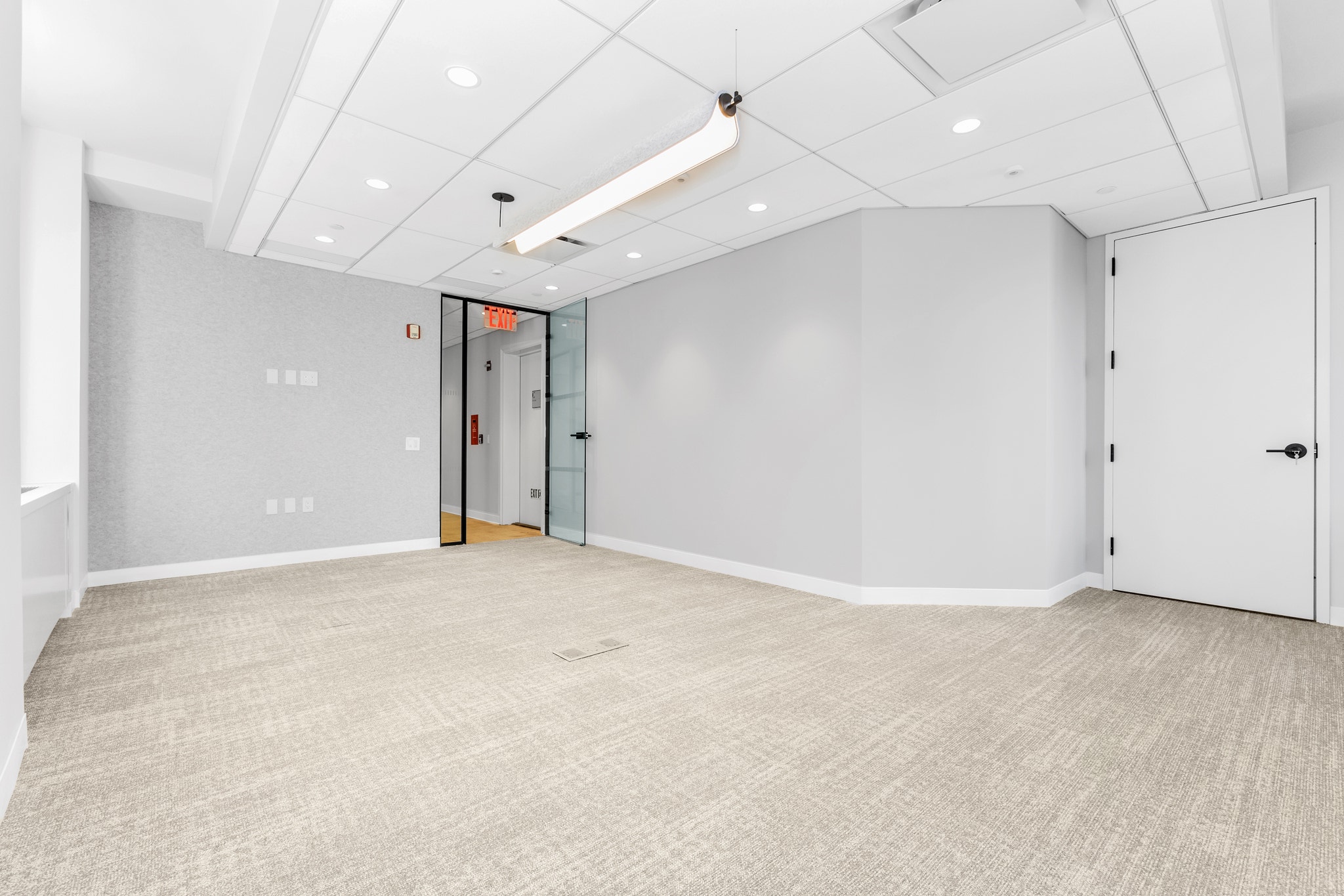 Empty carpeted office room with glass door entry and linear pendant light fixture