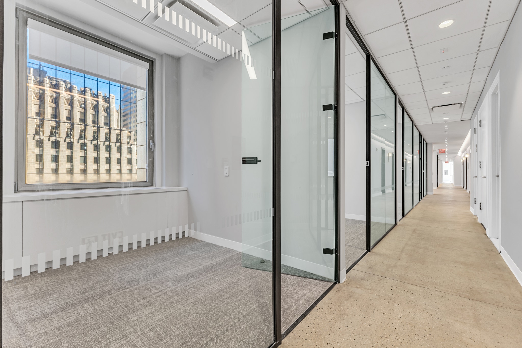 Glass-walled corridor with frosted door, city window view, and long hallway to private offices