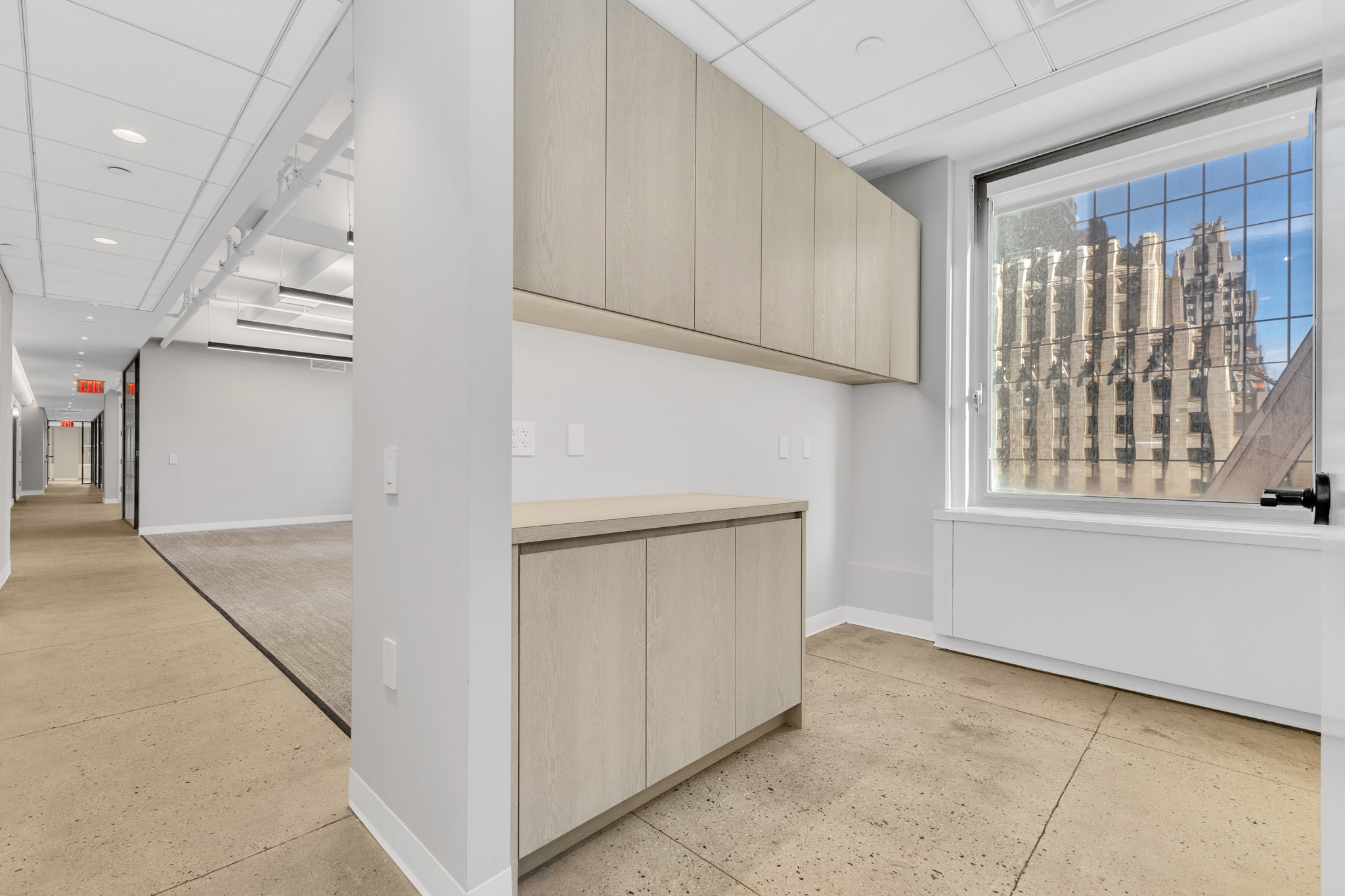 Built-in credenza with light wood cabinets beneath window overlooking city facade