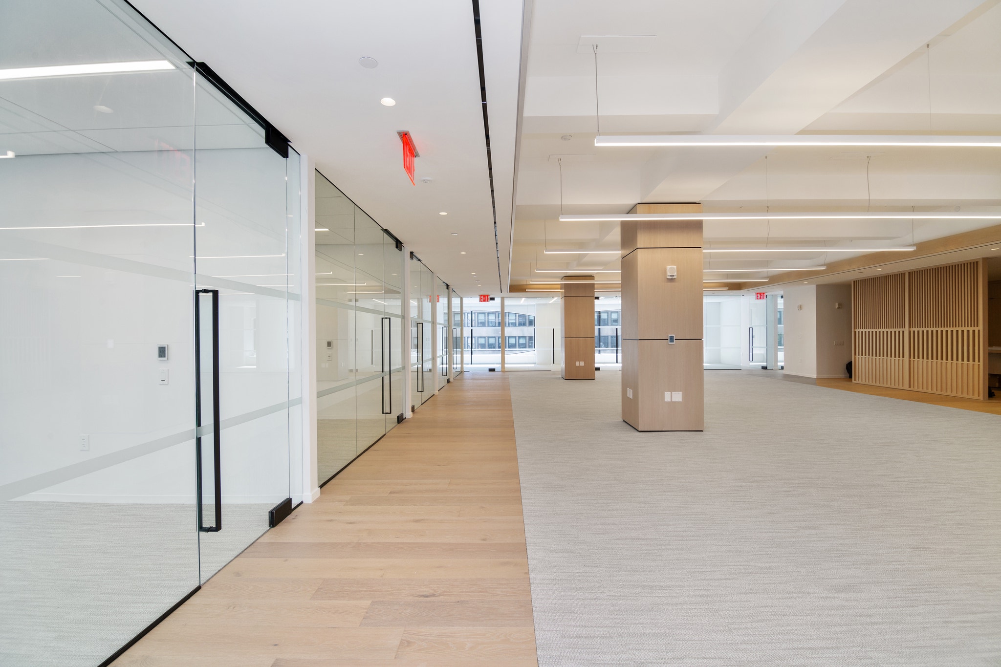 Corridor past frosted glass offices toward open floor with wood columns and slat wall accent