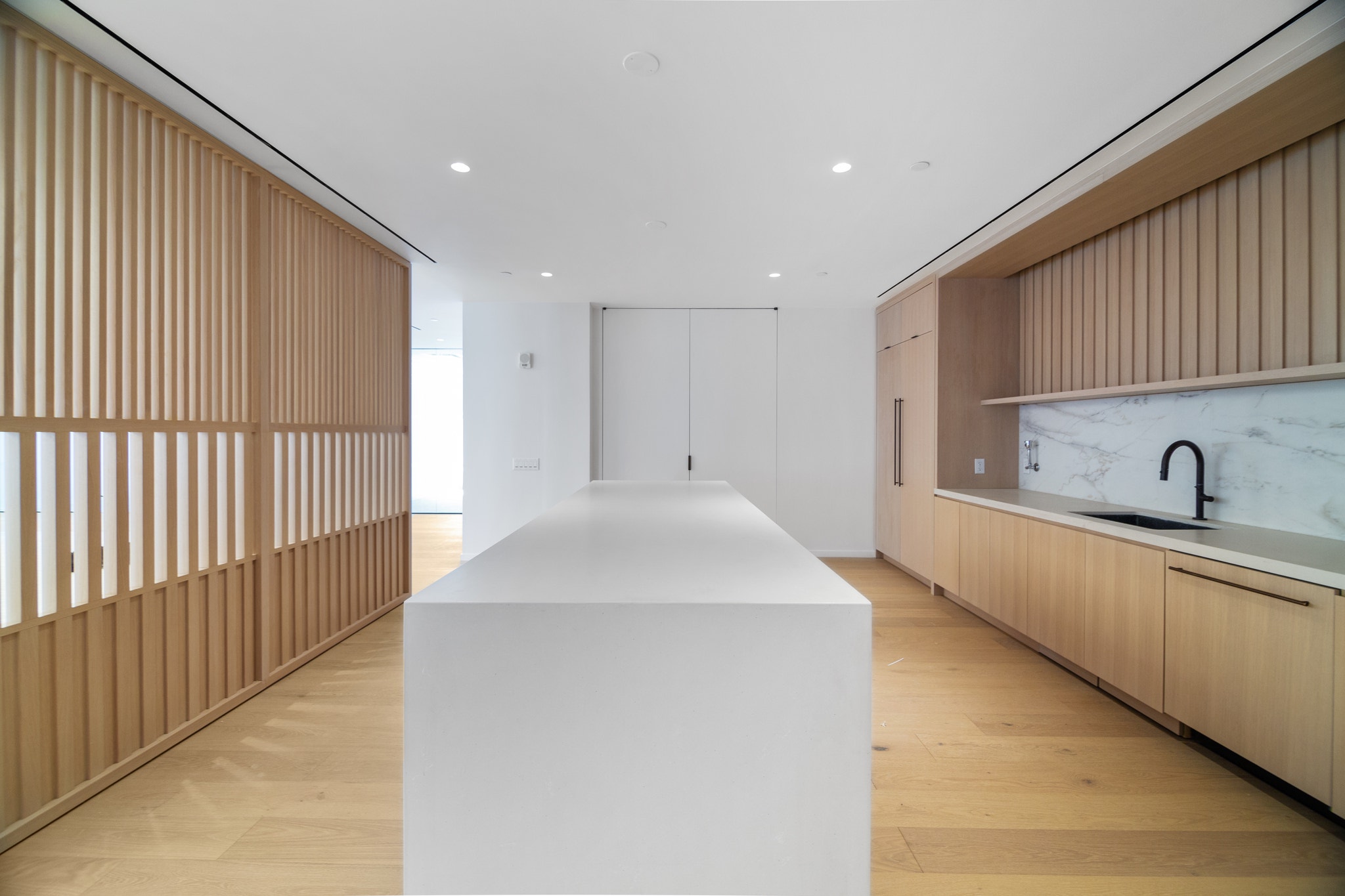 Wood slat partition wall dividing open floor from kitchenette with marble backsplash