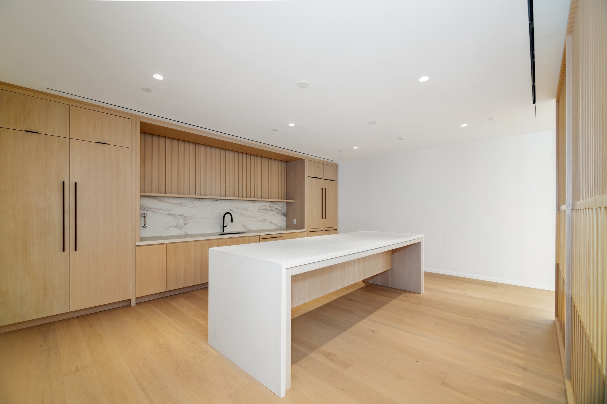 Light wood kitchenette with marble backsplash, black fixtures, and long island table