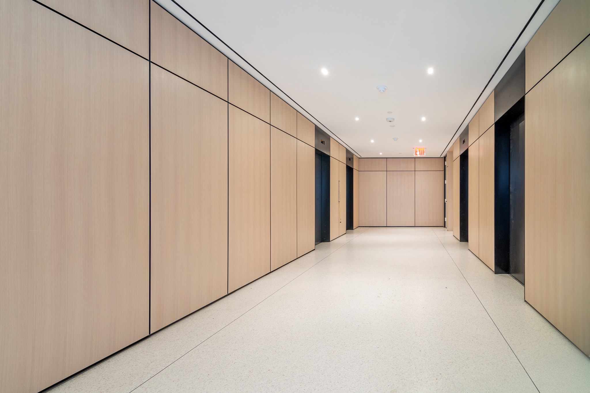 Elevator lobby corridor with light wood paneled walls and terrazzo flooring