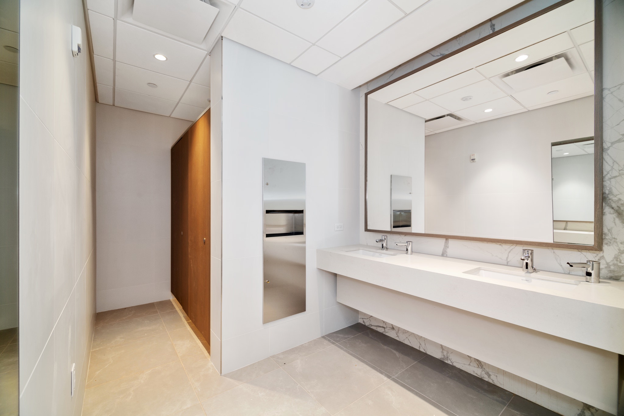 Modern restroom with marble-framed mirror, dual sink vanity, and wood stall partition