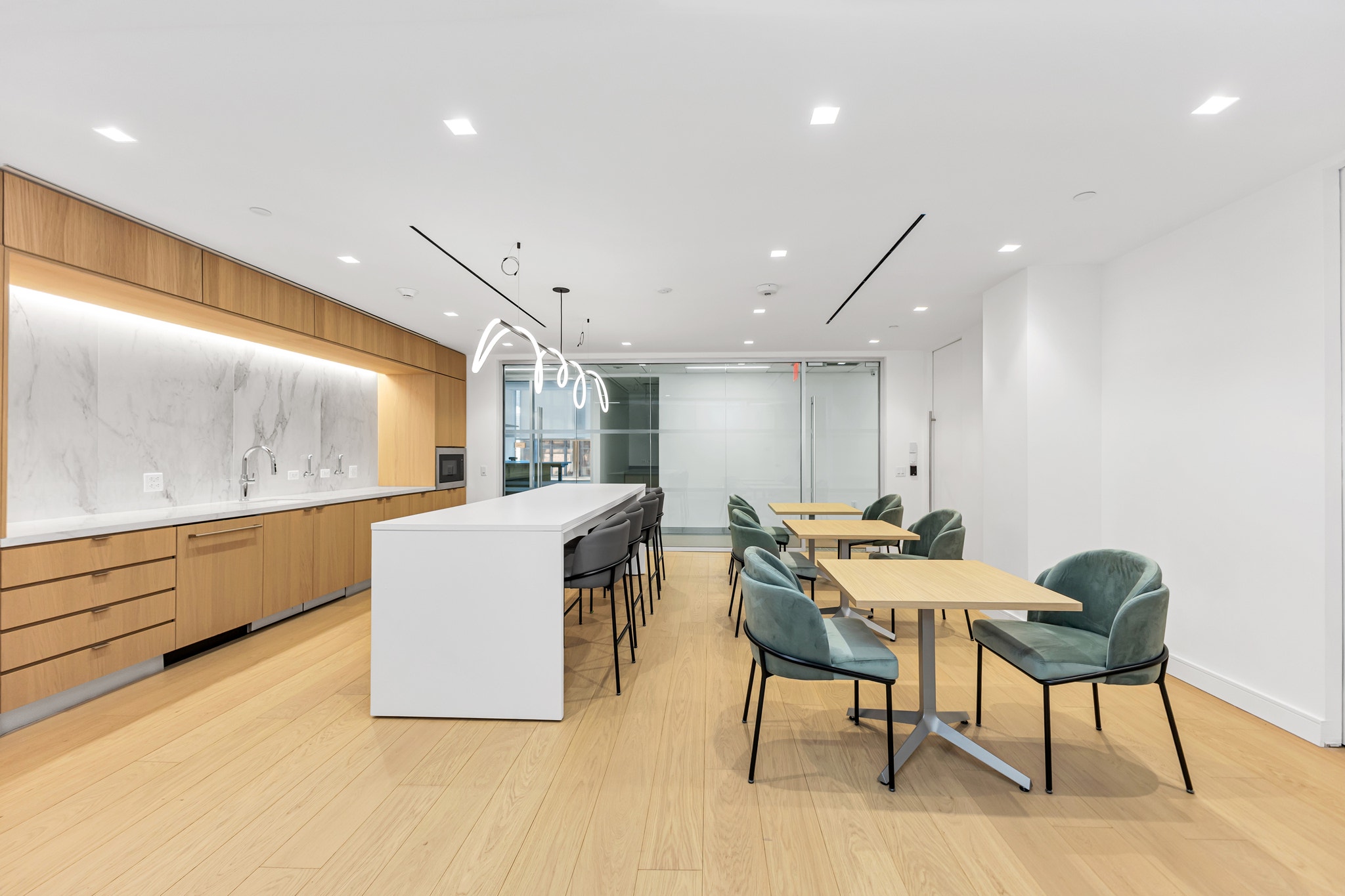 Office kitchen with marble backsplash, wood cabinetry, white island seating, and green velvet dining chairs