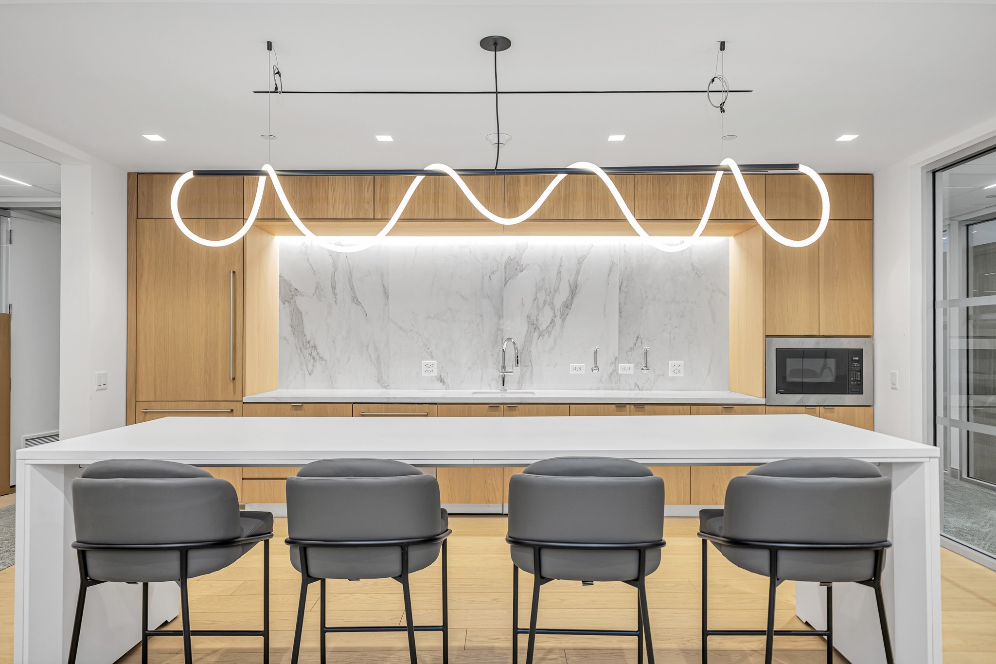 Wavy LED pendant light above white kitchen island with gray barstools and marble slab backsplash