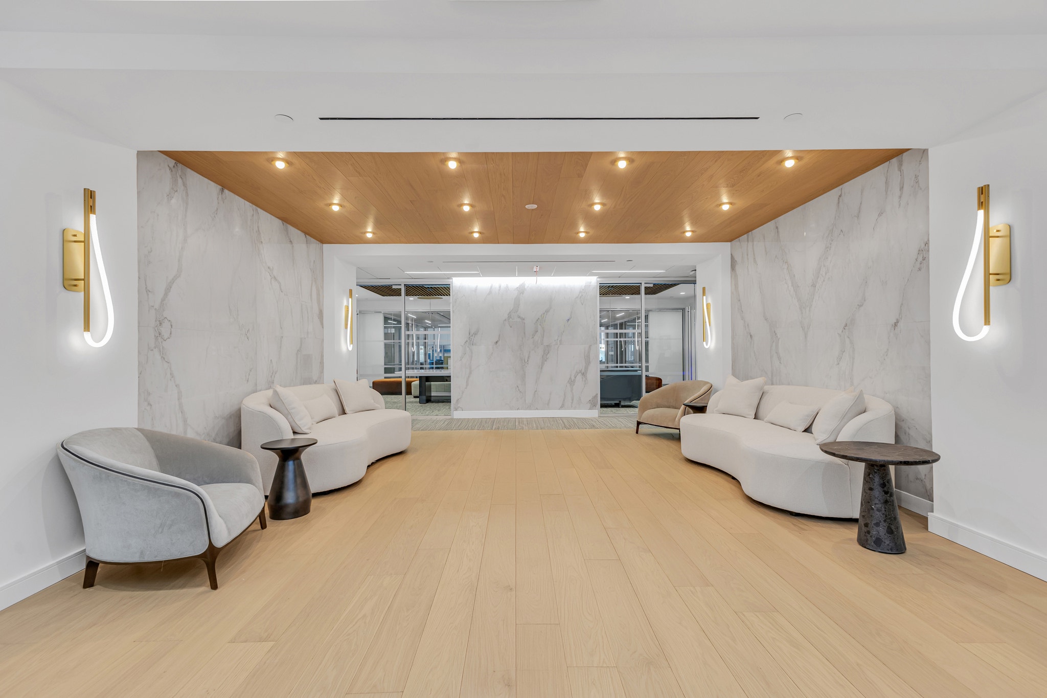 Lounge area with curved white sofas, gray velvet chairs, marble accent wall, and brass wall sconces